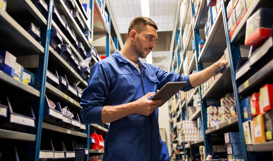 Automotive parts specialist checks inventory on a tablet in a dealership parts warehouse.